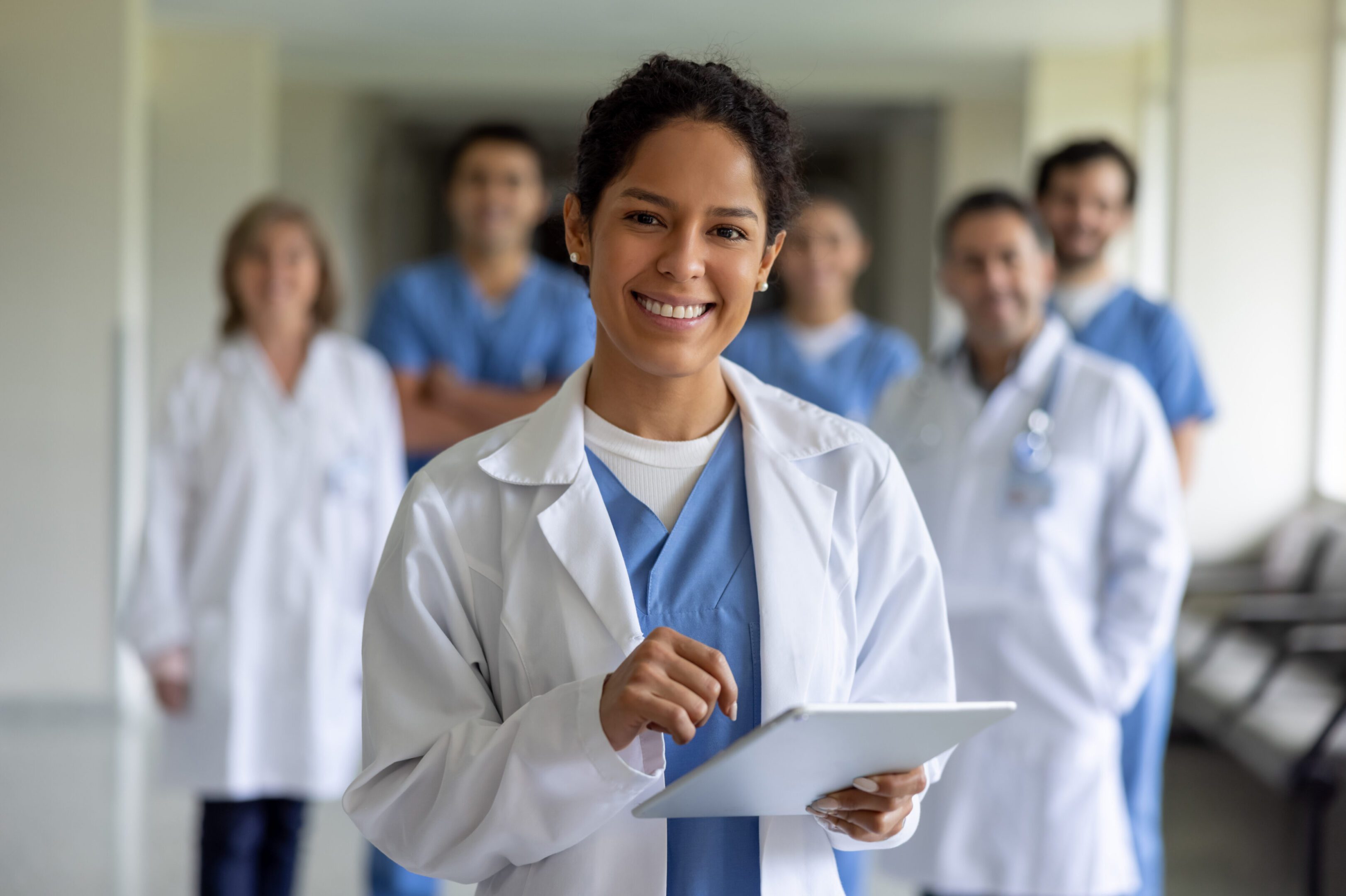 Smiling doctor holding tablet with team behind.